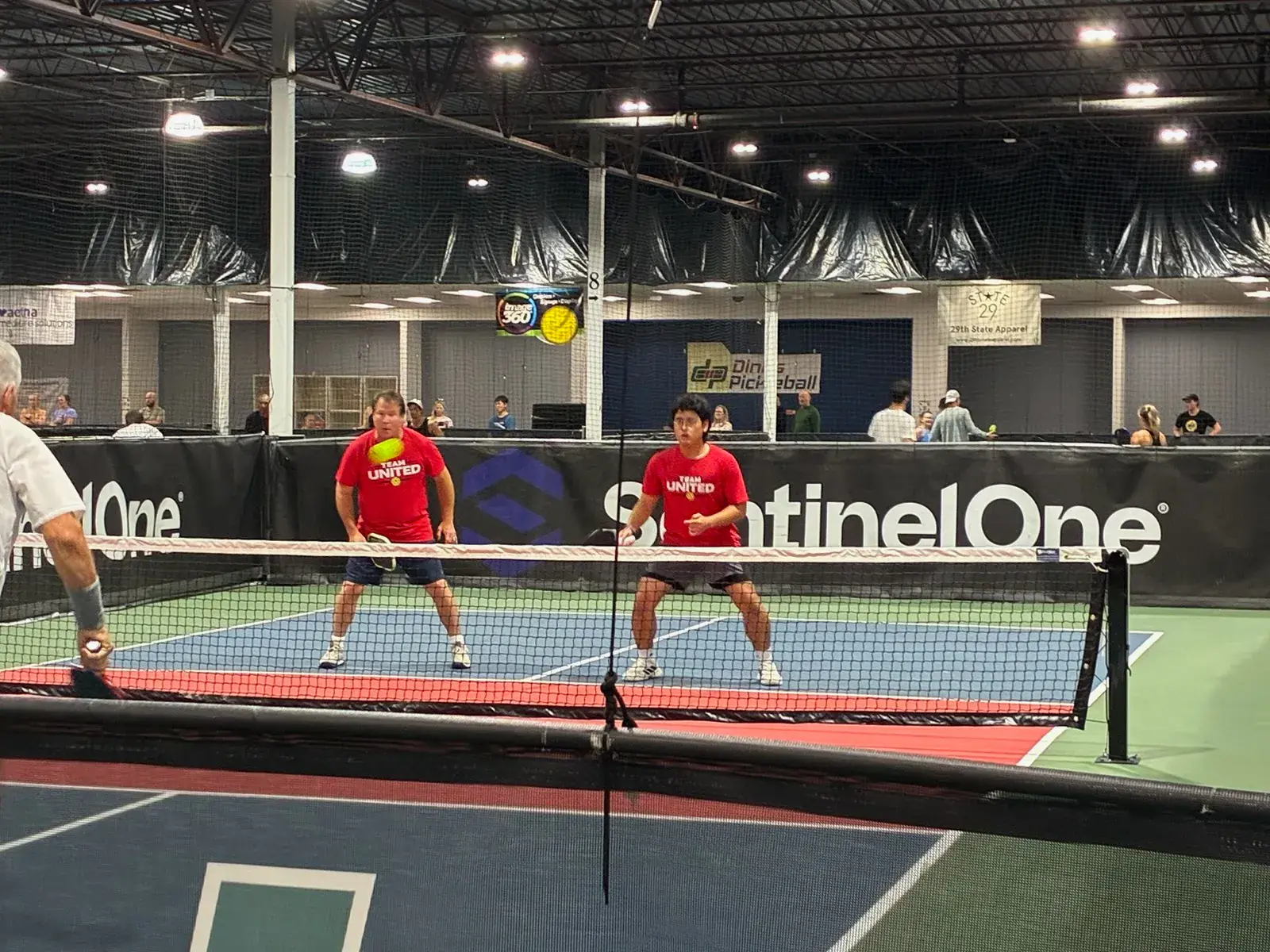 Coach Mark Boehm and his doubles partner in Team United shirts, ready at the net during a tournament match