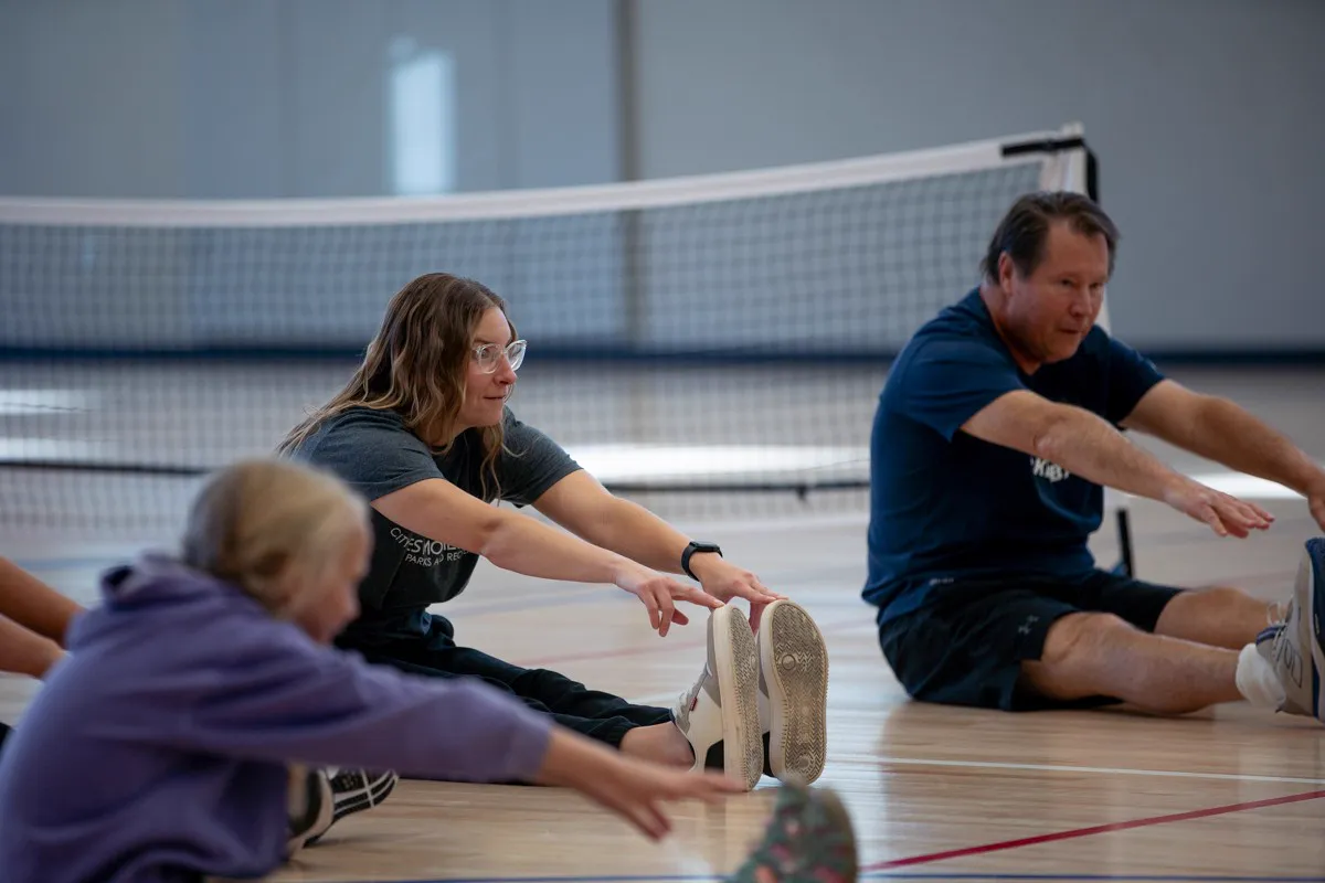 Coach Mark Boehm stretching on the gym floor with players before a session