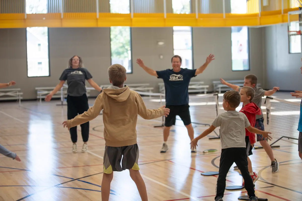 Coach Mark Boehm leading a group of young players through jumping jacks in a gym